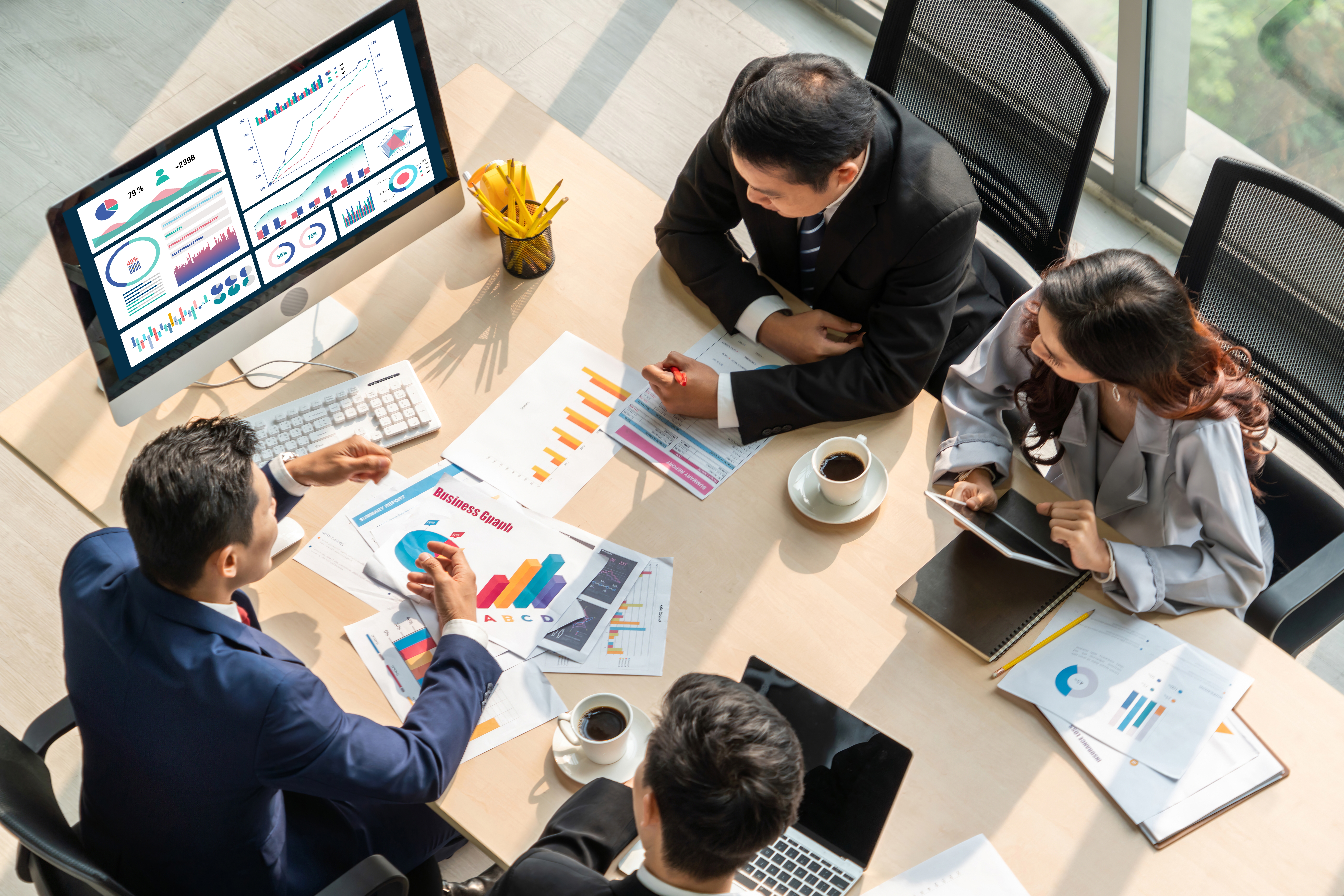 A business team having a meeting while analyzing data and charts on a computer screen and documents on a table.