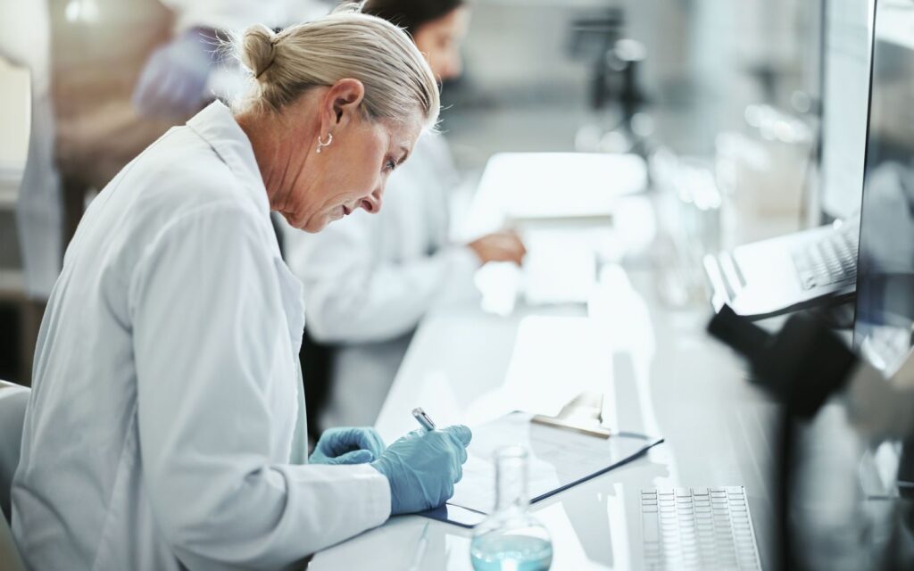 A scientist in a lab writing on a clipboard with a flask, conducting research in a professional laboratory setting.