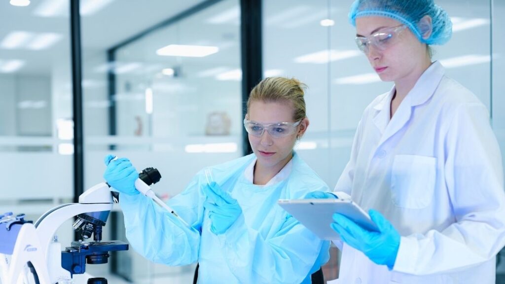 Batch Record Review Process for FDA-Regulated Manufacturers 7 Image shows two scientists in a lab coats, gloves, and safety goggles working with a microscope and a tablet. The keyword for this is FDA-Regulated Manufacturers.
