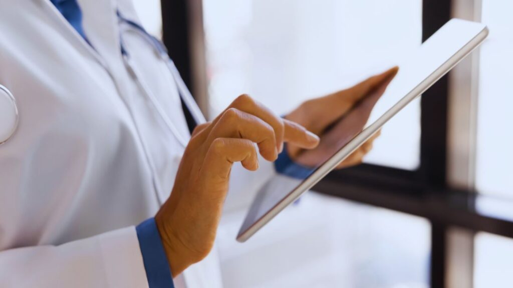 Paper vs Electronic Batch Records: Compliance, Costs & What to Choose 6 Close-up of doctor in white coat with stethoscope tapping on tablet screen, highlighting digital healthcare tools.