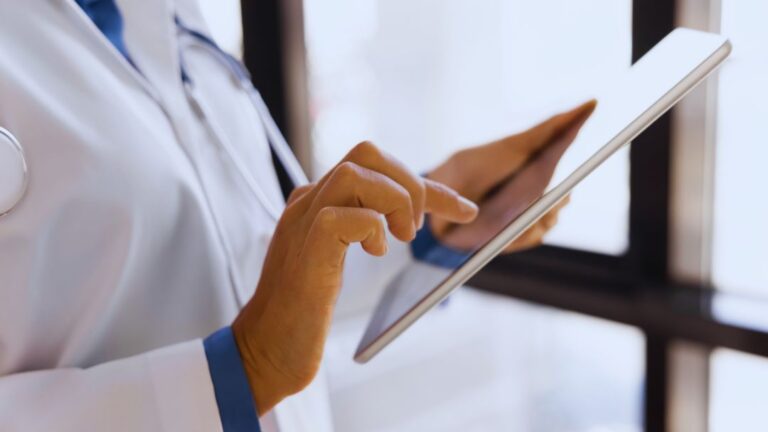 Life Science Project Management Consulting 22 Close-up of doctor in white coat with stethoscope tapping on tablet screen, highlighting digital healthcare tools.