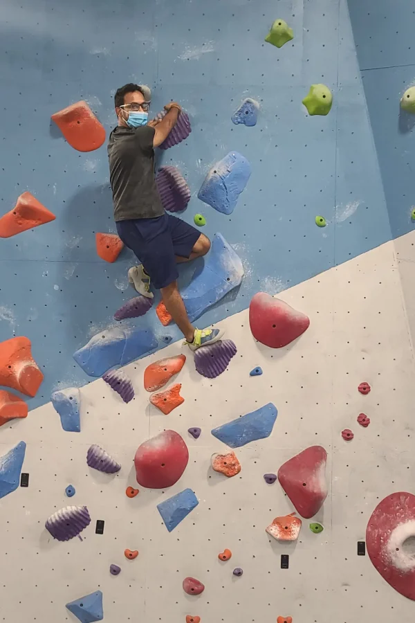 Man rock climbing on an indoor wall while wearing a mask