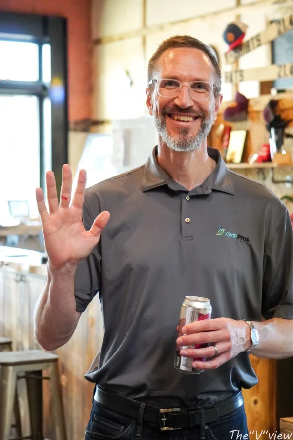 Smiling man waving while holding a drink at a GMP Pros event