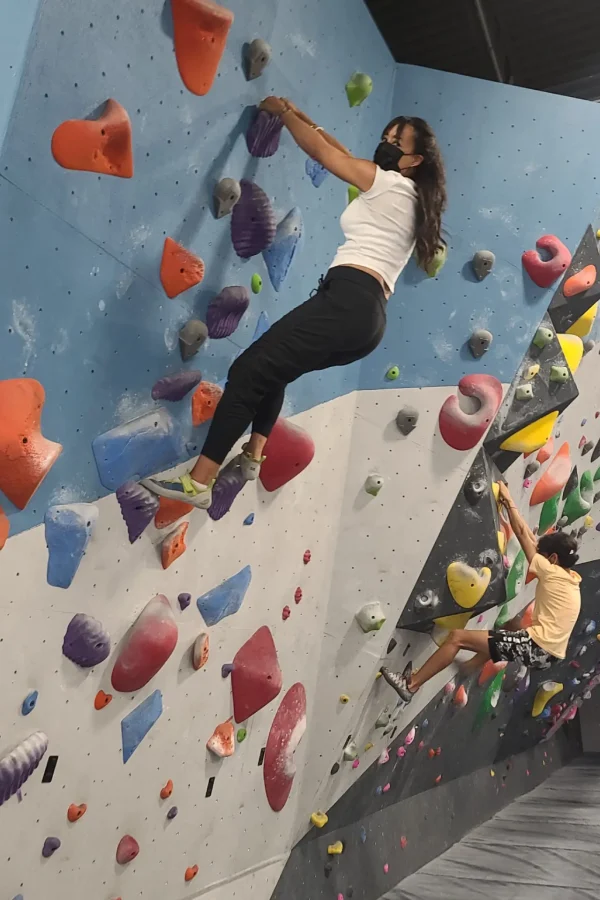 Woman climbing an indoor rock wall while wearing a mask